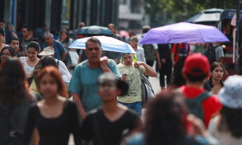 People cover themselves with umbrellas next to others as they walk along a sidewalk during high temperatures, in Mexico City, Mexico May 9, 2024. REUTERS/Henry Romero